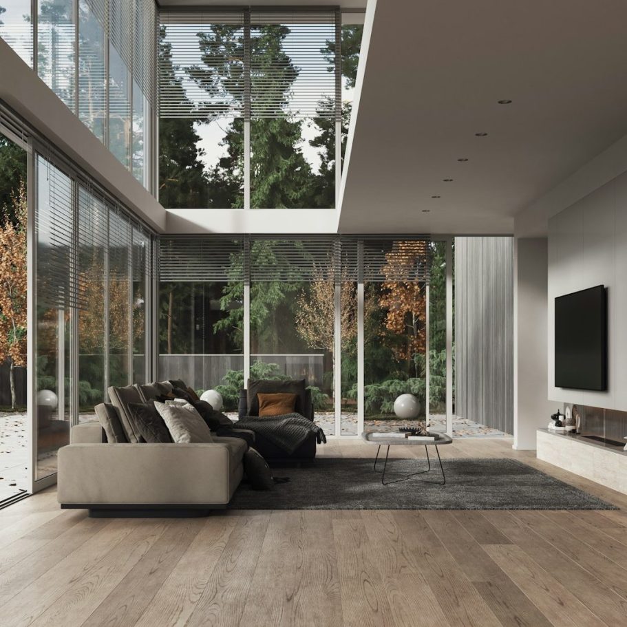 Salon moderne avec de grandes fenêtres, canapé beige et télévision murale.