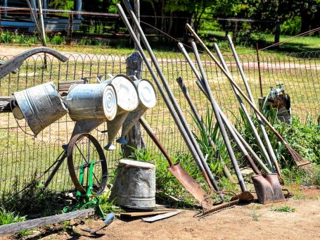 Outils de jardinage variés alignés contre une clôture en bois, avec des seaux et des pelles.