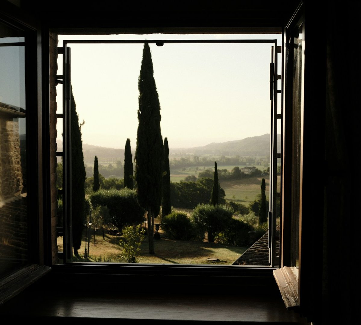Vue d'une vallée à travers une fenêtre ouverte, avec des cyprès au premier plan. Vue d'une vallée à travers une fenêtre ouverte, avec des cyprès au premier plan.
